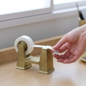 Hand using a roll of tape on a wooden surface Brass Desktop Tape Dispenser Small - FUTAGAMI
